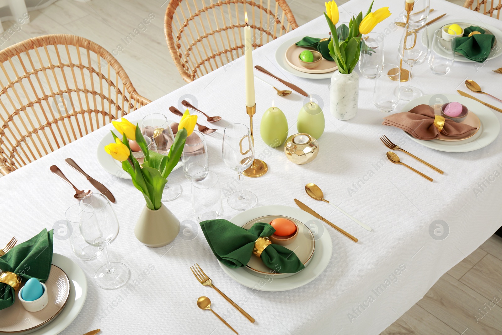 Photo of Festive Easter table setting with painted eggs, burning candles and yellow tulips indoors