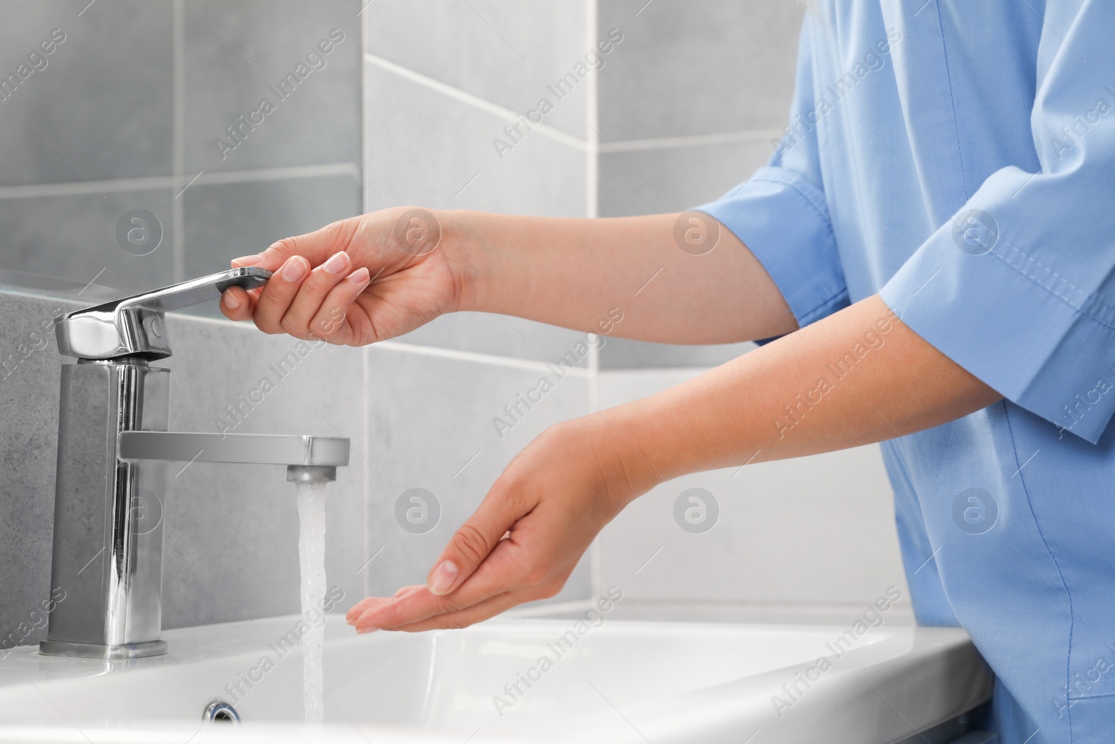 Photo of Doctor washing hands with water from tap in bathroom, closeup