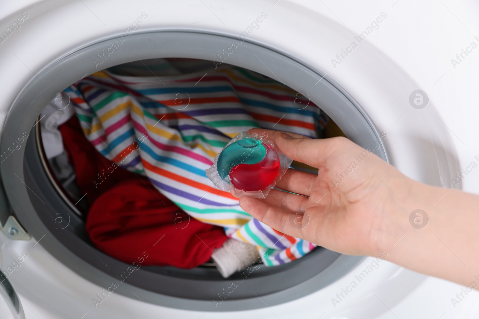 Photo of Woman putting laundry detergent capsule into washing machine, closeup