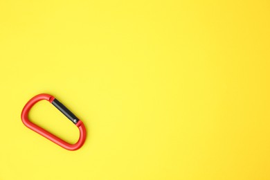 Photo of One red carabiner on yellow background, top view. Space for text