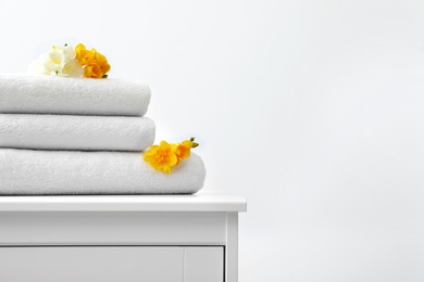 Photo of Stack of fresh towels with flowers on cabinet against white background. Space for text