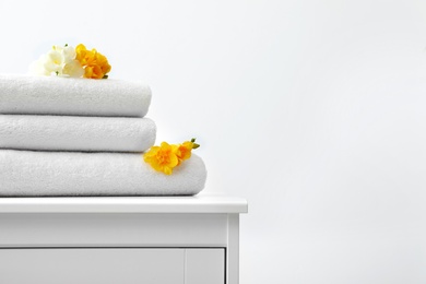 Stack of fresh towels with flowers on cabinet against white background. Space for text