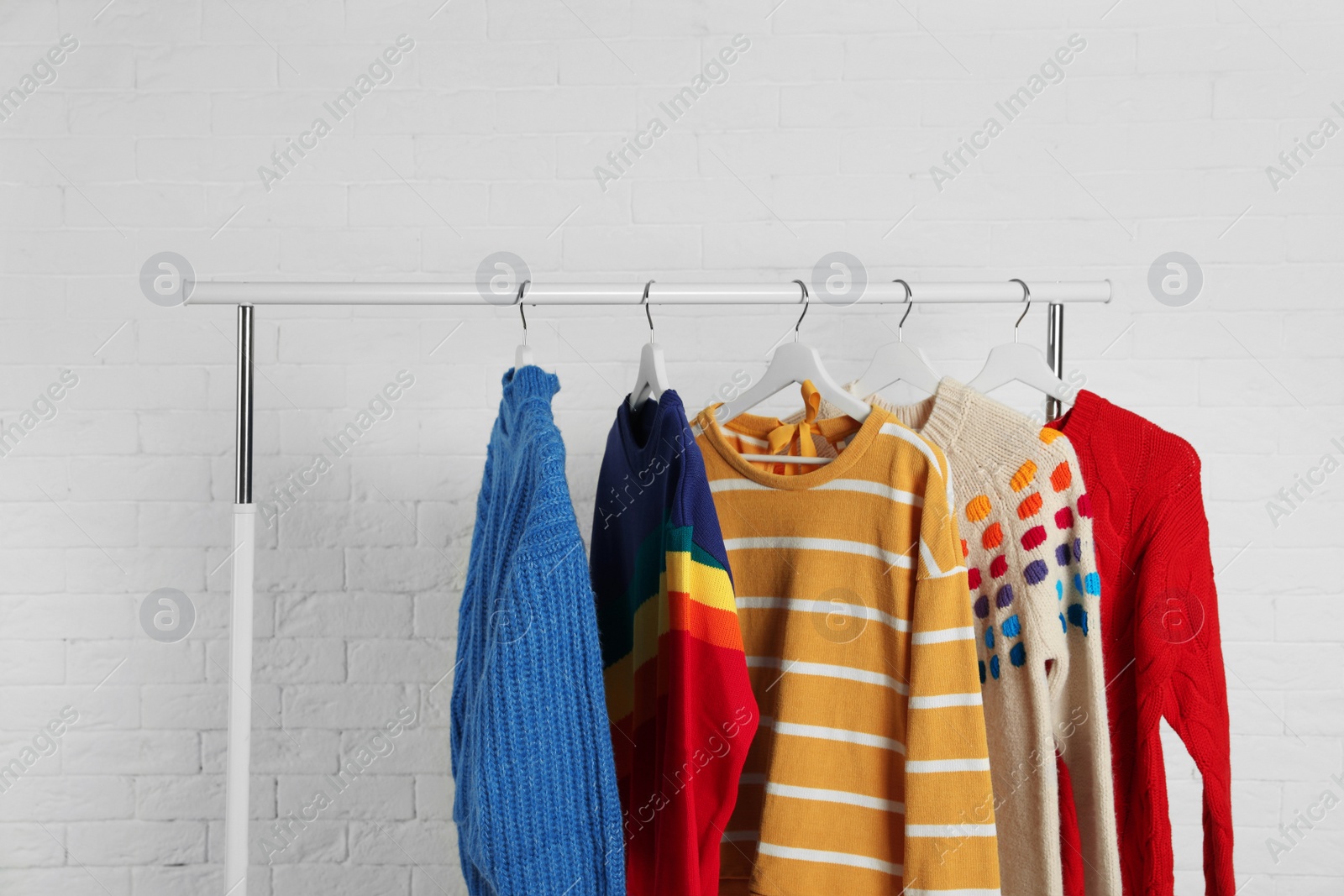 Photo of Collection of warm sweaters hanging on rack against white brick wall