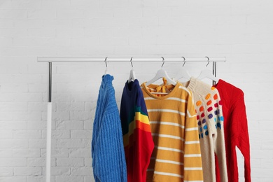 Collection of warm sweaters hanging on rack against white brick wall