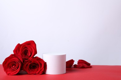 Photo of Stylish presentation for product. Round podium, beautiful roses and petals on red table against white background, space for text