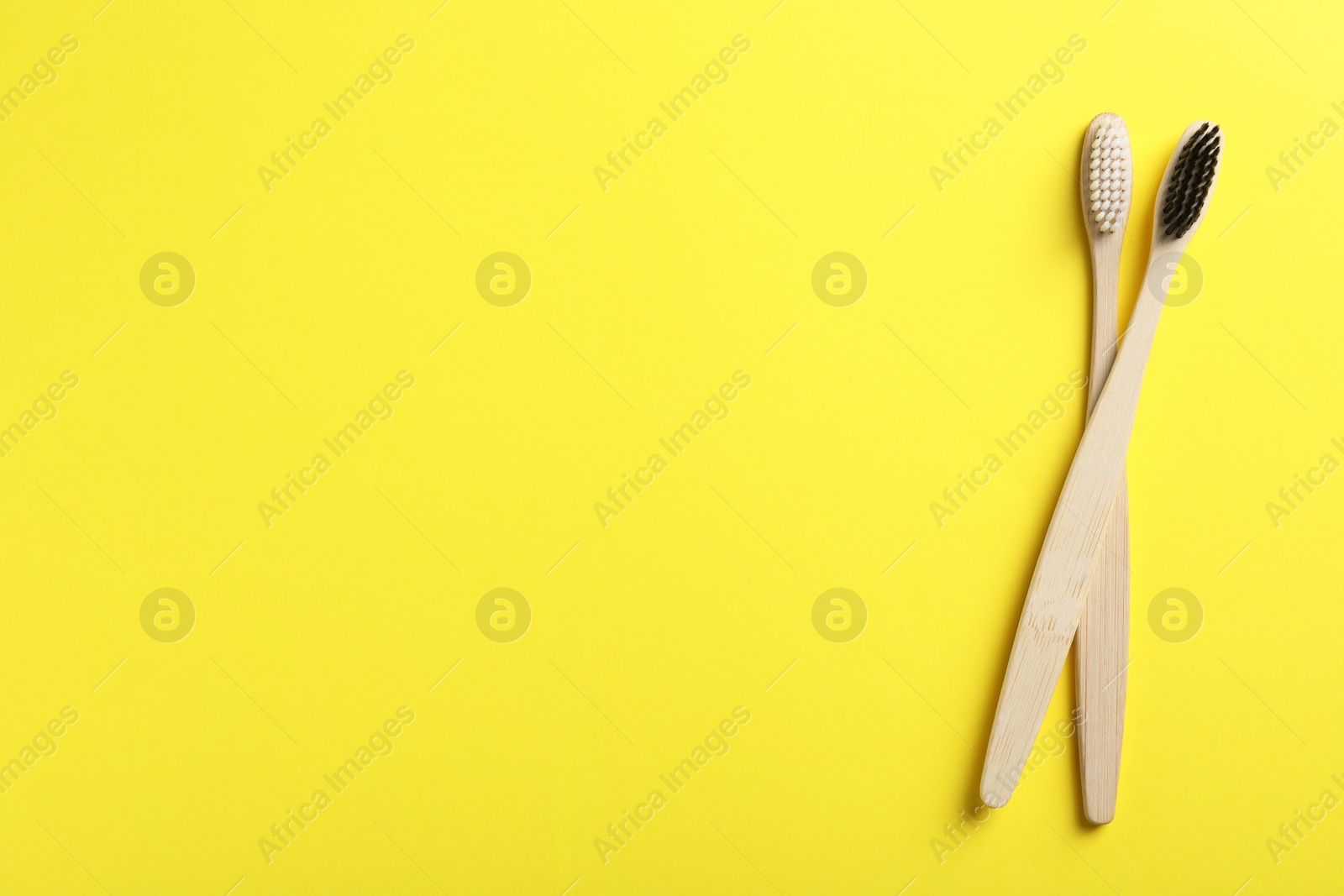 Photo of Two bamboo toothbrushes on yellow background, flat lay. Space for text