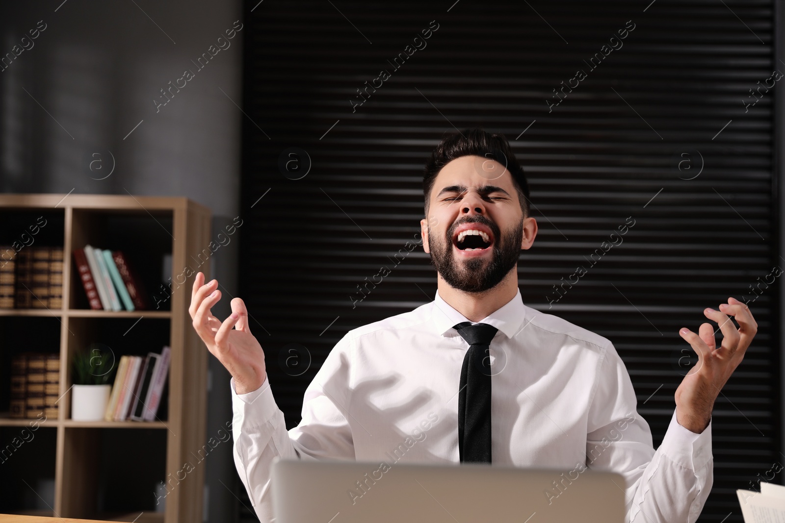 Photo of Emotional young businessman working on laptop in office. Online hate concept