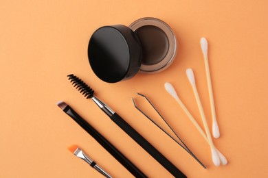 Eyebrow pomade with henna effect and professional tools on orange background, flat lay