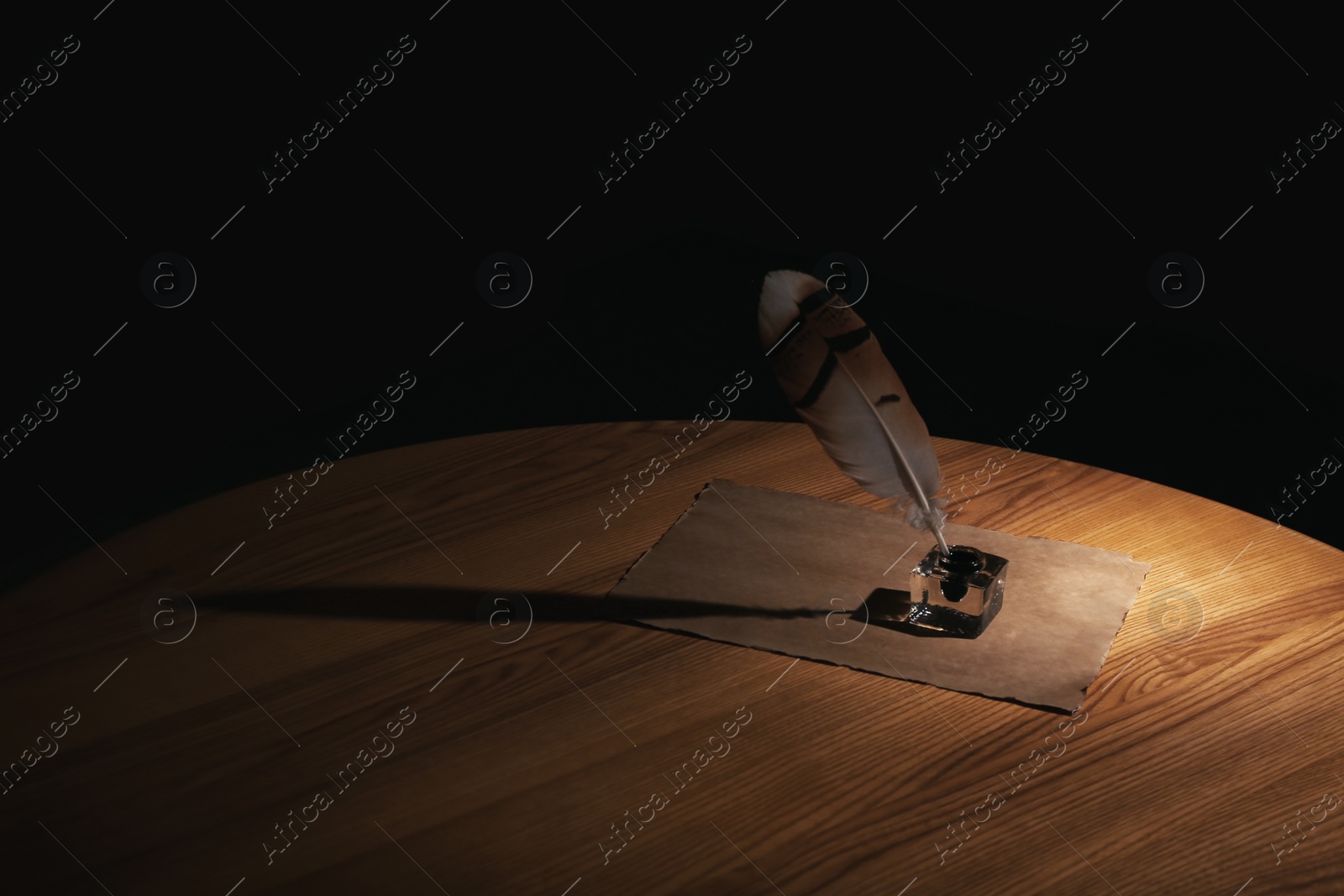 Photo of Feather pen, inkwell and blank parchment on table in darkness. Space for text