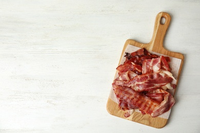 Photo of Slices of tasty fried bacon on white wooden table, top view. Space for text