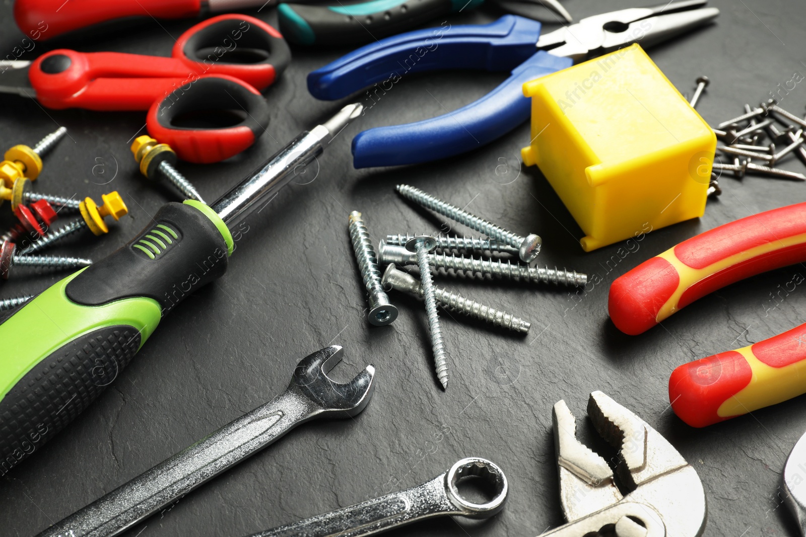 Photo of Pliers, screwdriver, wrenches and other tools for repair on black textured table, closeup