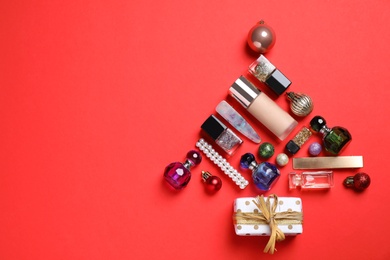 Photo of Christmas tree made of cosmetic products, accessories and baubles on red background, flat lay. Space for text