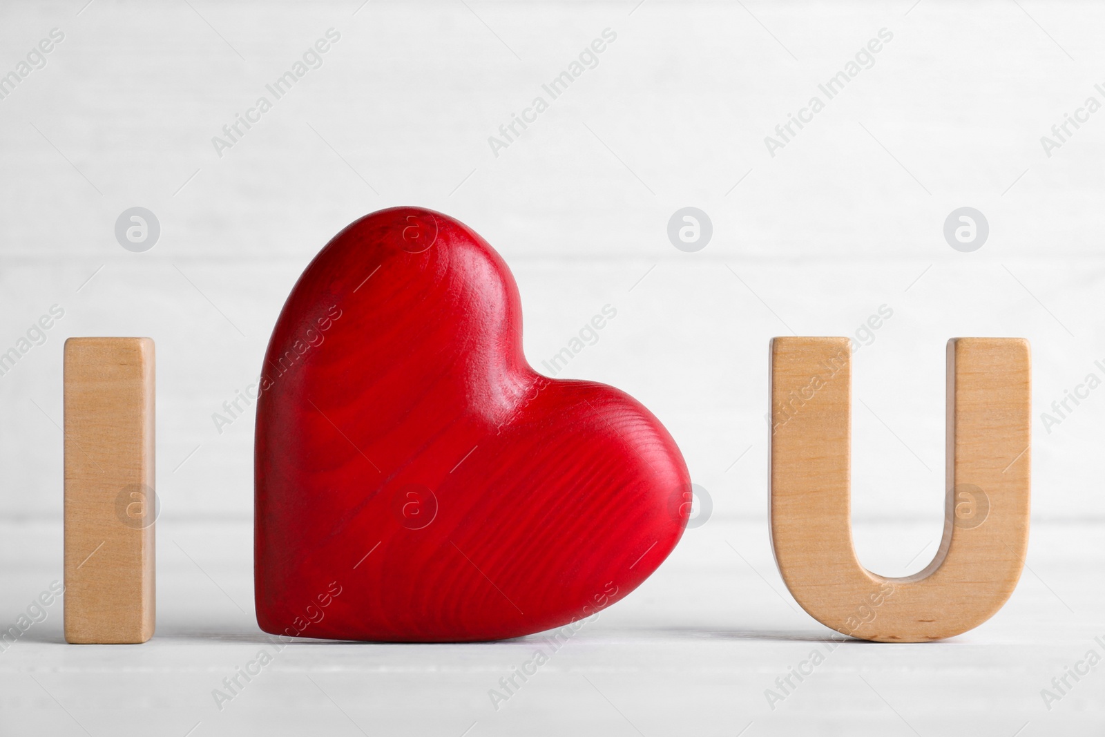 Photo of Phrase I Love You made of wooden letters and red heart on white table