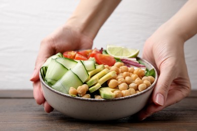 Photo of Woman holding bowl of delicious salad with chickpeas and vegetables at wooden table, closeup