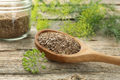 Photo of Spoon with dry seeds and fresh dill on wooden table, closeup