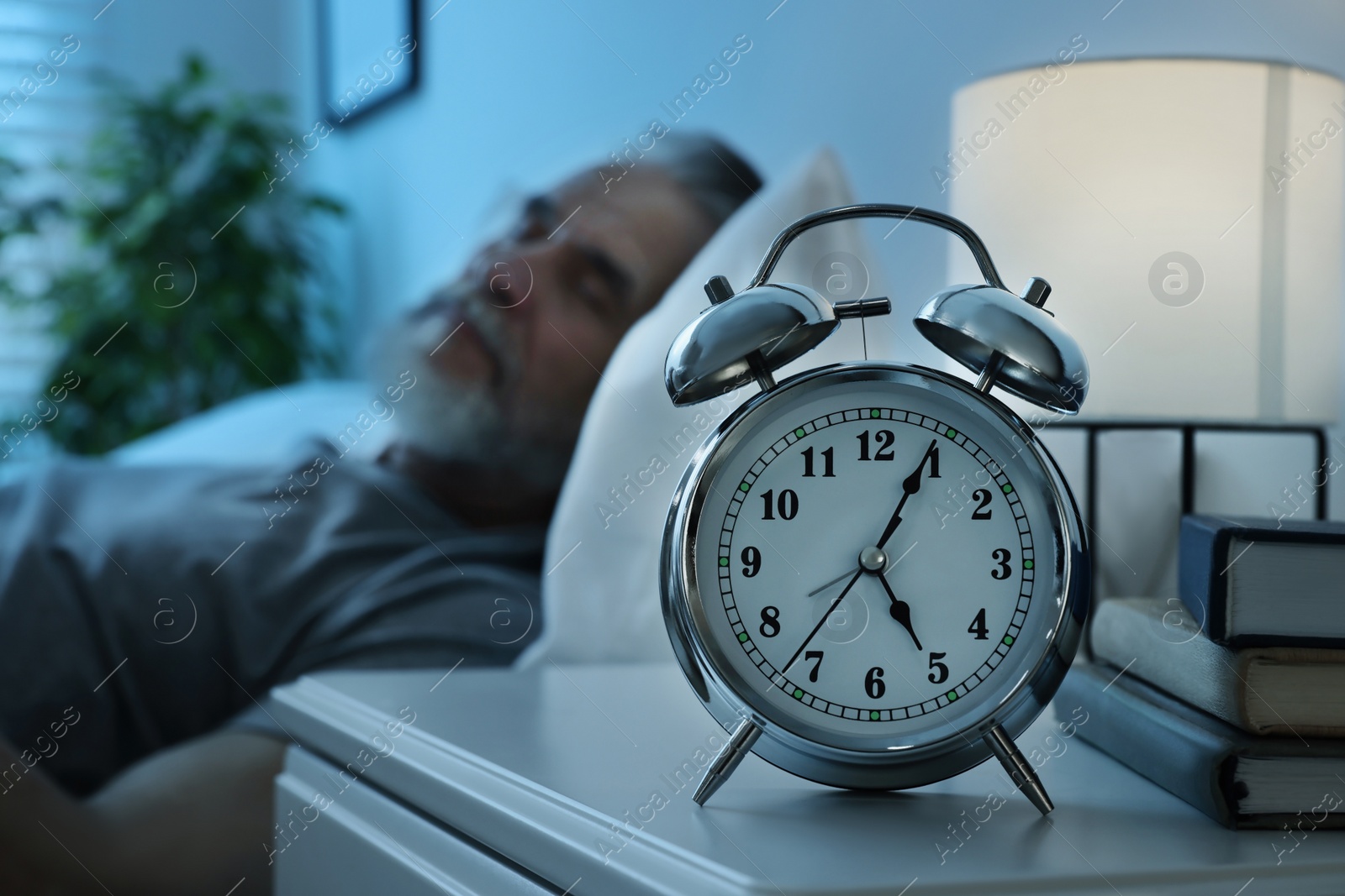 Photo of Senior man sleeping in bed at home, focus on alarm clock. Space for text