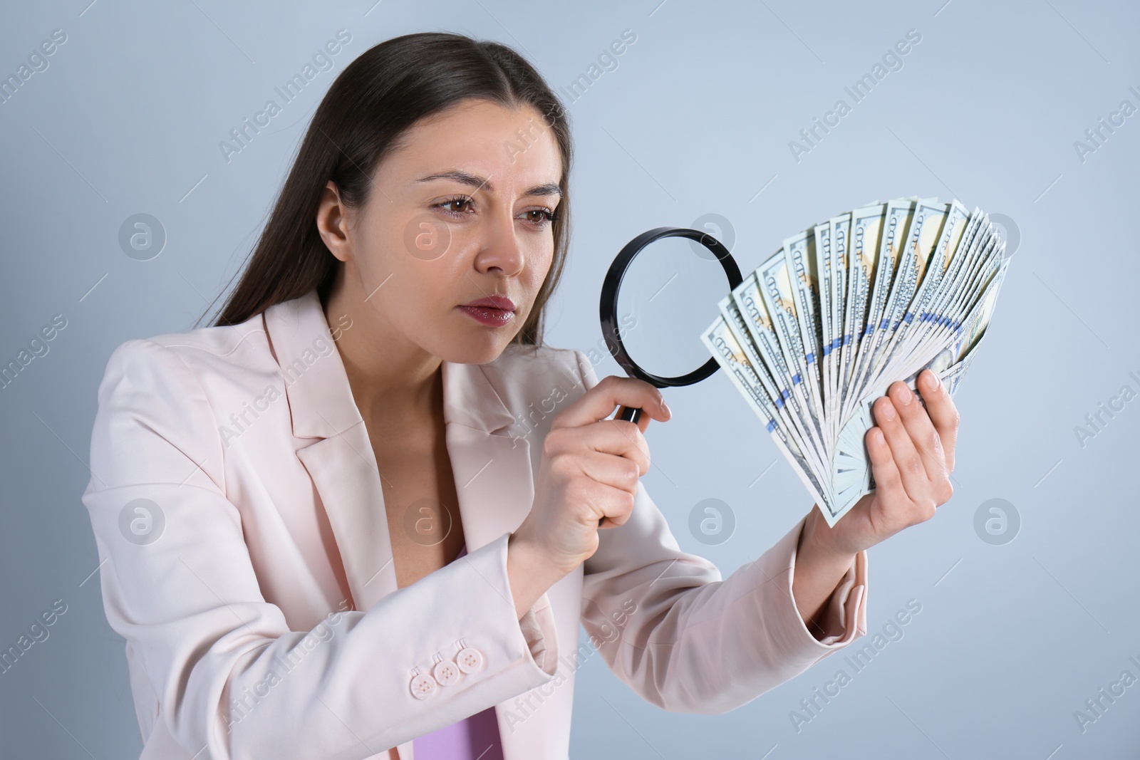 Photo of Expert authenticating 100 dollar banknotes with magnifying glass on light grey background. Fake money concept