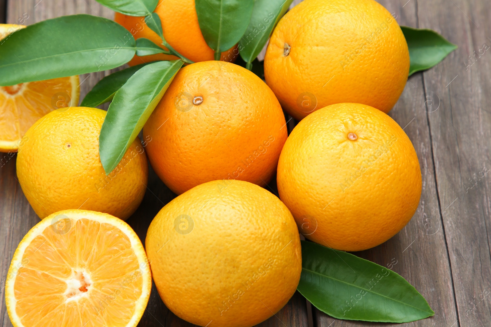 Photo of Many ripe oranges and green leaves on wooden table, closeup