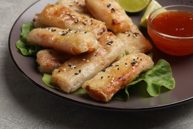 Photo of Tasty fried spring rolls with lettuce and sauce on gray table, closeup