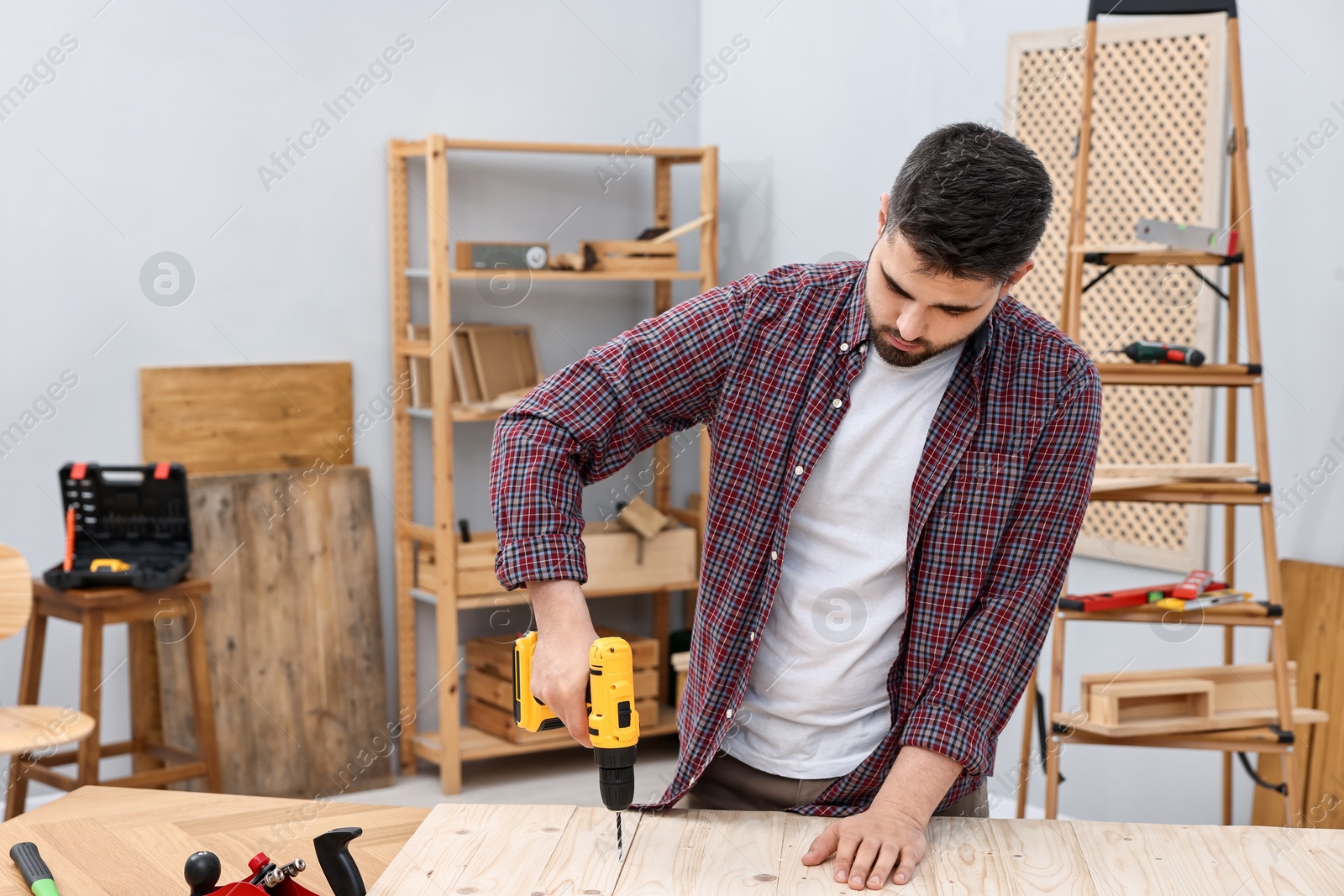 Photo of Young handyman working with electric drill at table in workshop