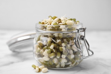 Photo of Glass jar with sprouted green mung beans on white marble table, closeup