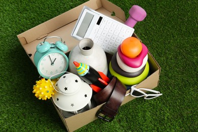 Photo of Box with different stuff on green grass. Garage sale