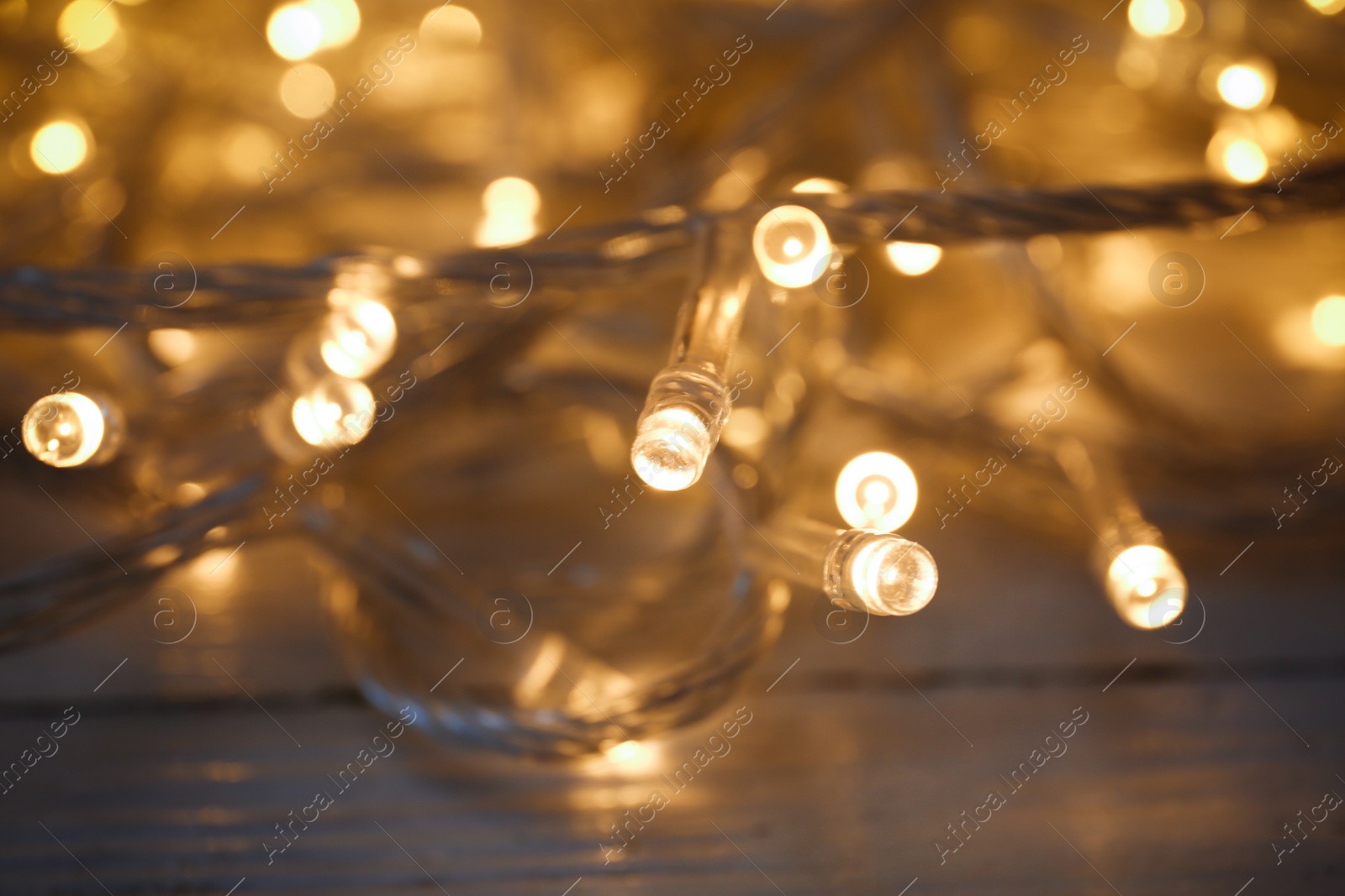 Photo of Glowing Christmas lights on white wooden background, closeup