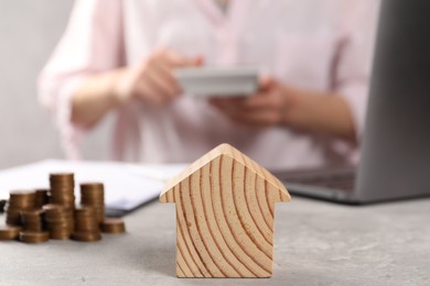 Photo of Woman calculating money at grey table, focus on wooden house model