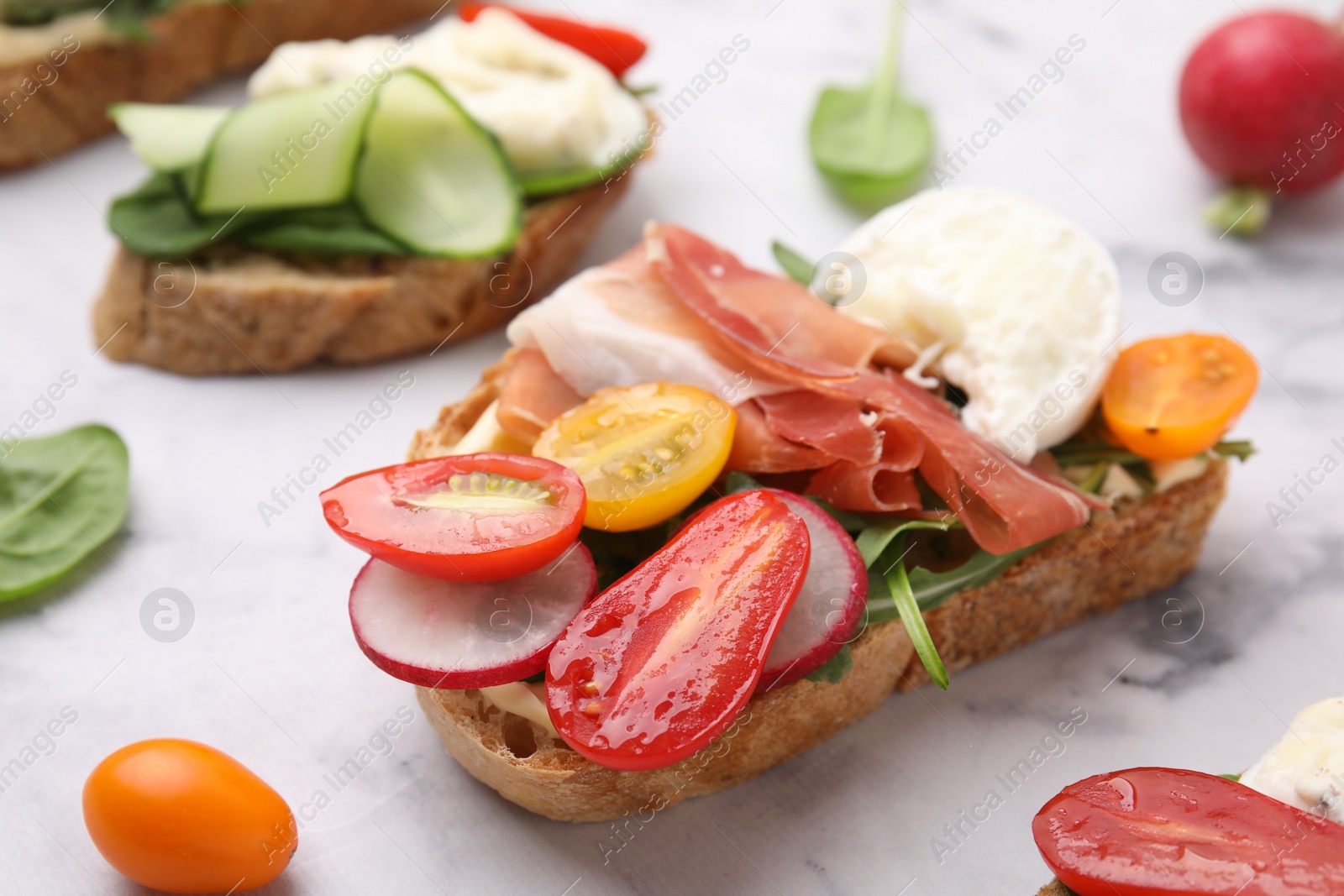 Photo of Delicious sandwich with burrata cheese, ham, radish and tomatoes on white marble table, closeup