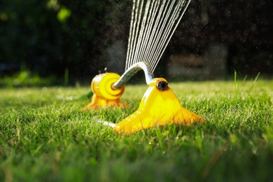 Photo of Automatic sprinkler watering green grass on lawn in garden, closeup. Irrigation system