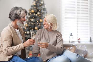 Happy mature couple with glasses of champagne celebrating Christmas at home