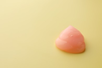 Photo of Sample of pink face cream on yellow background, space for text