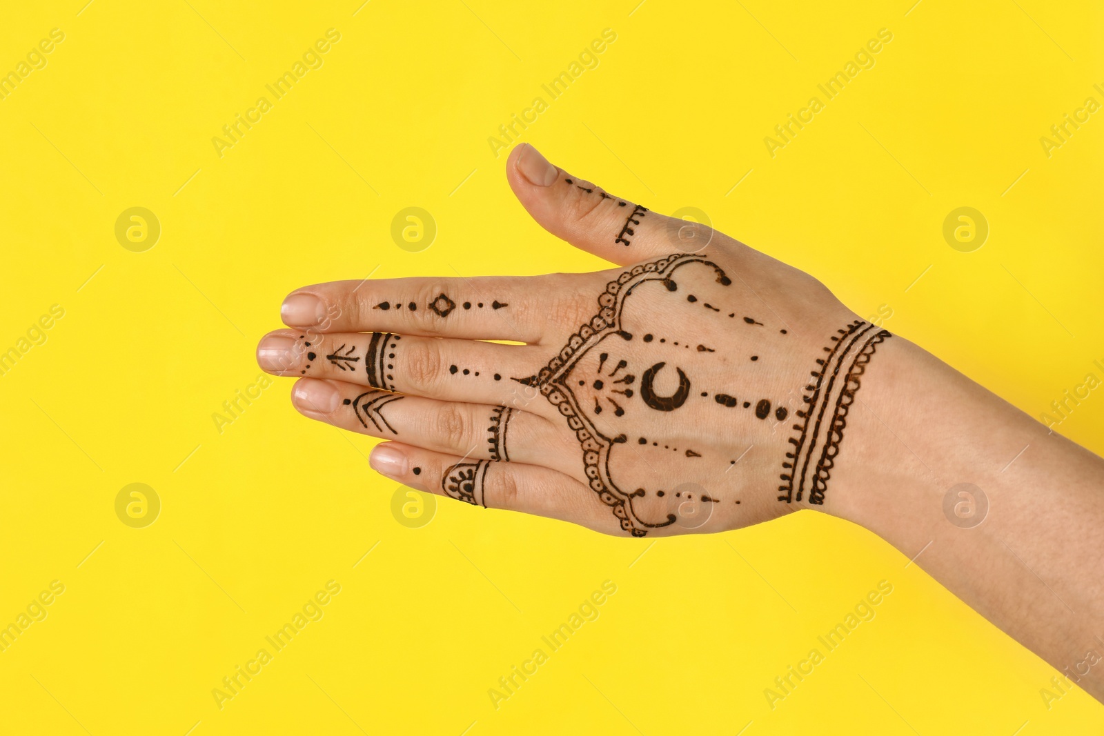 Photo of Woman with henna tattoo on hand against yellow background, closeup. Traditional mehndi ornament