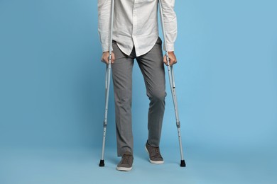 Man with crutches on light blue background, closeup