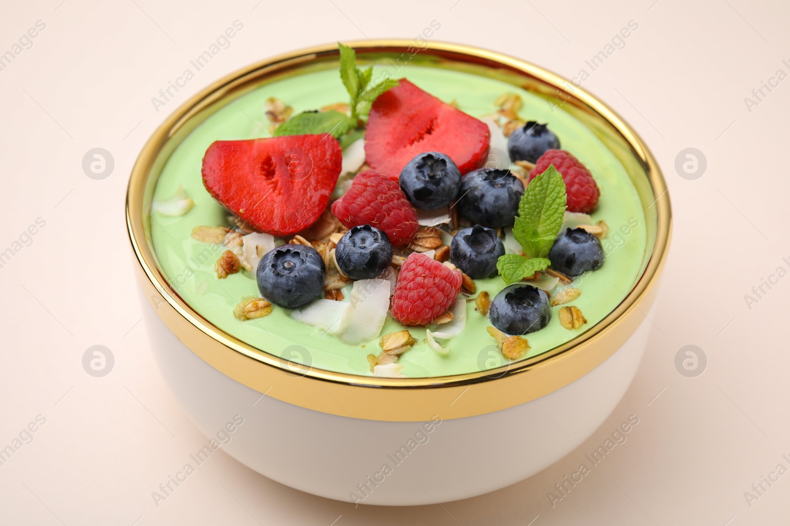 Photo of Tasty matcha smoothie bowl served with berries and oatmeal on beige background, closeup. Healthy breakfast
