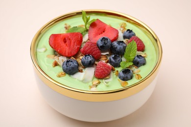 Tasty matcha smoothie bowl served with berries and oatmeal on beige background, closeup. Healthy breakfast