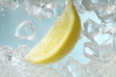 Photo of Juicy lemon slice and ice cubes in soda water against light blue background, closeup