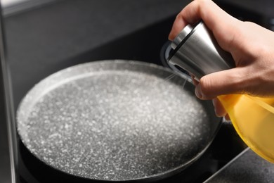 Woman spraying cooking oil onto frying pan on stove, closeup