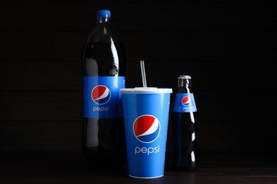 MYKOLAIV, UKRAINE - JUNE 9, 2021: Cup and bottles of Pepsi against black background