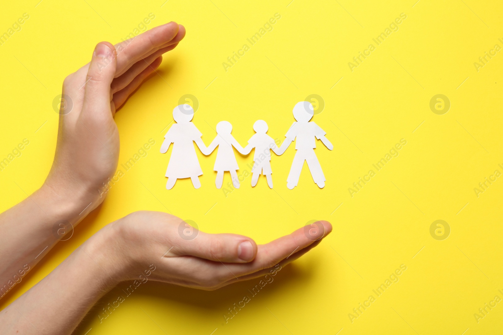 Photo of Woman protecting paper cutout of family on yellow background, top view. Space for text