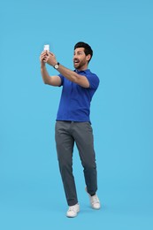 Photo of Happy man taking selfie with smartphone on light blue background