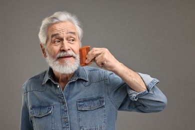 Senior man combing beard on grey background
