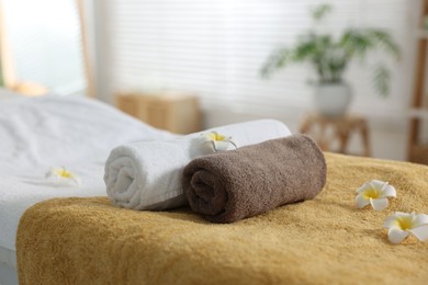 Photo of Massage table with towels and flowers in spa center, closeup