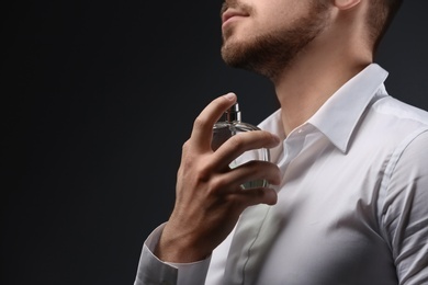 Handsome man in shirt using perfume on dark background, closeup