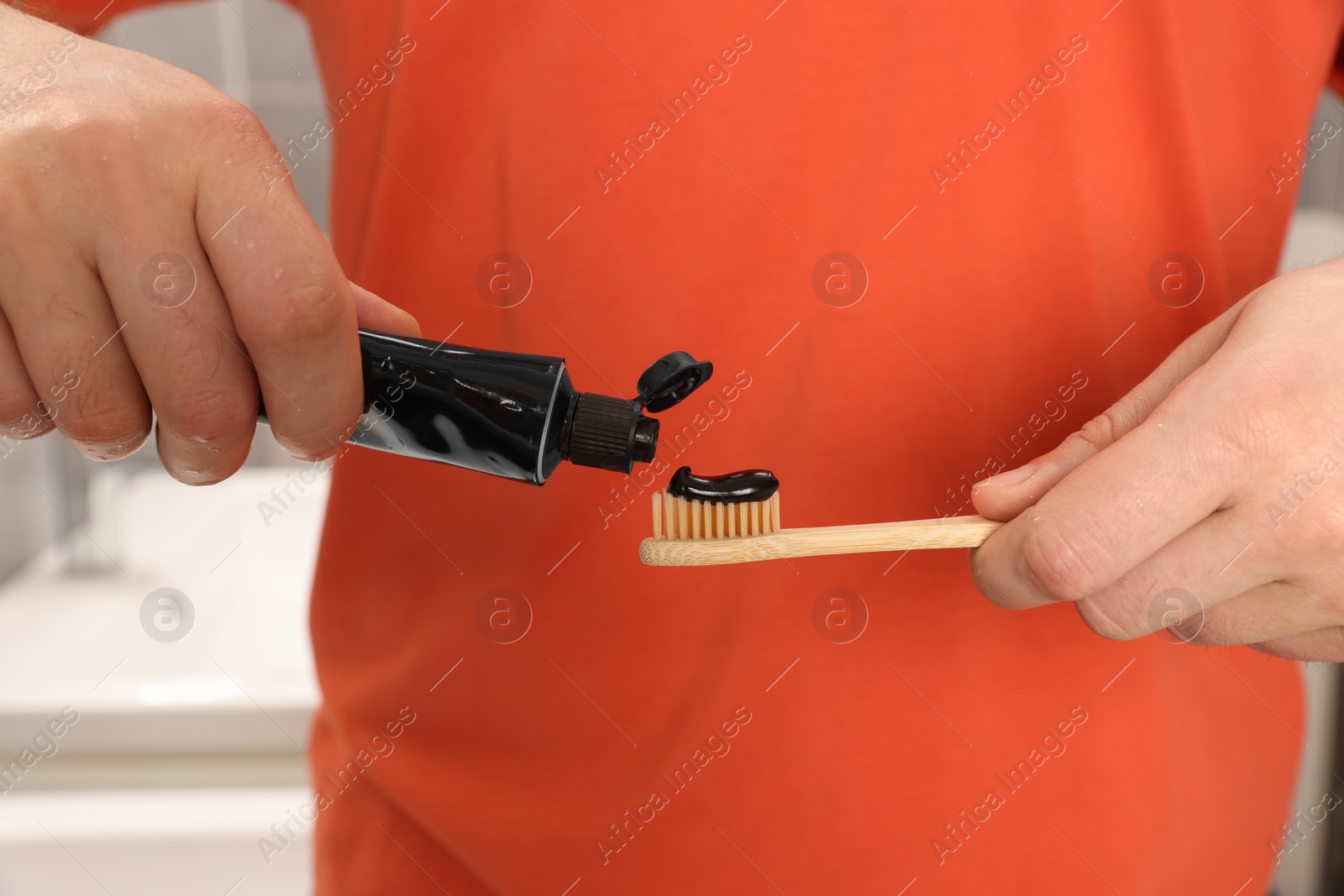 Photo of Man applying charcoal toothpaste onto toothbrush in bathroom, closeup