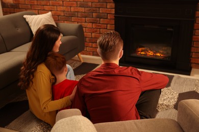 Happy family spending time together on floor near fireplace at home, back view