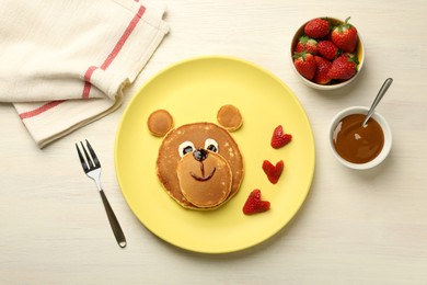 Photo of Creative serving for kids. Plate with strawberries, cute bear made of pancakes on light wooden table, flat lay