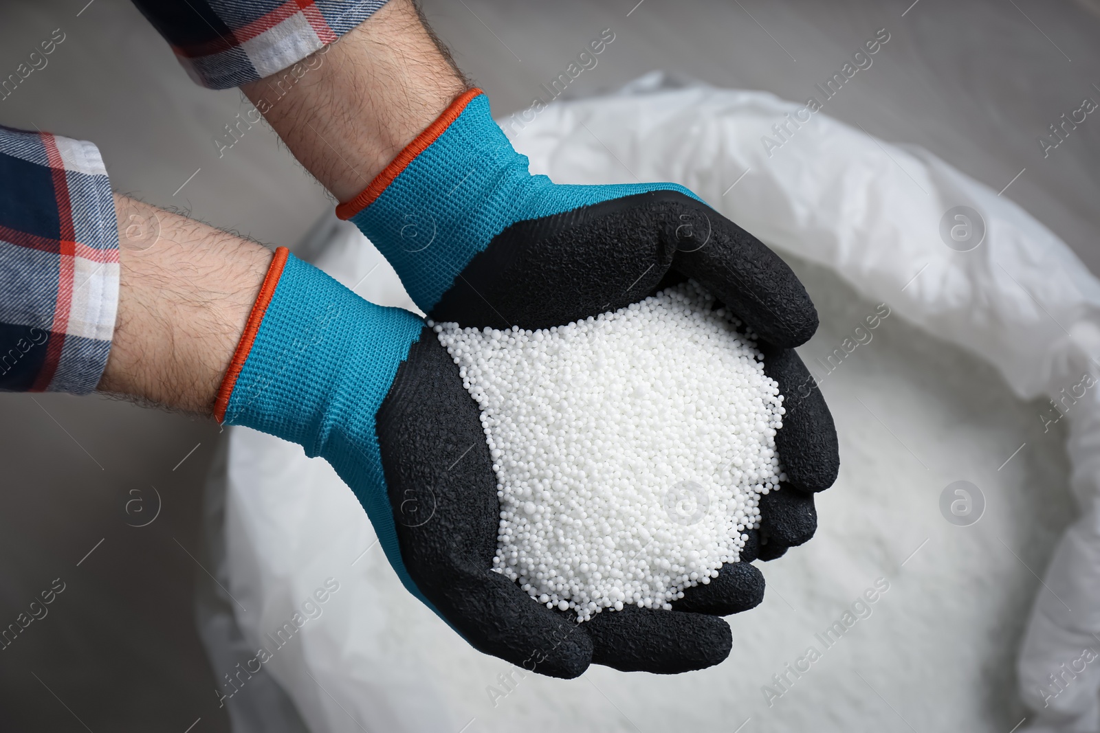 Photo of Farmer holding pile of ammonium nitrate pellets over bag, top view. Mineral fertilizer