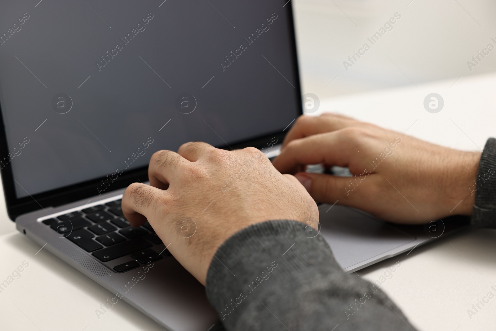 Photo of E-learning. Young man using laptop at white table, closeup