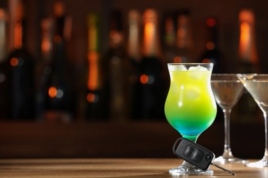 Photo of Car key and glass of alcoholic drink on table against blurred background, space for text. Drunk driving concept